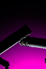 Two microphones are positioned close together against a dark background. Purple light casts a striking glow, highlighting their outlines and details.