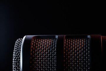 A microphone sits against a dark background. Light reflects off its surface, showing the details of its mesh and casing. The focus is on the microphone's textures and shapes.
