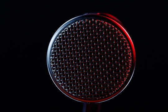 A microphone is centered in the frame against a dark background. Light reflects off its surface, revealing patterns and textures as it stands still.