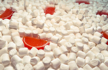 Food, sweets. Scattered white marshmallows and slices of orange marmalade.