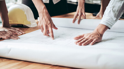 People reviewing architectural plans on a worktable with safety helmets nearby.