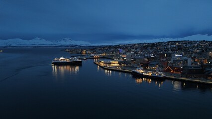 Naklejka premium Beautiful night drone picture of Tromsø's harbor, while a boat is maneuvering to safely get to shore, during a lovely spring evening with all the lights on.