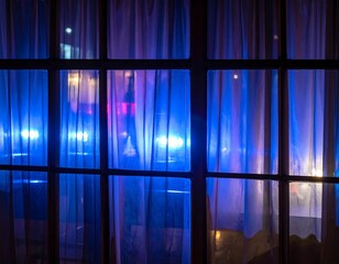Through a window pane, translucent curtains reveal blurred lights and shapes at nighttime, possibly reflecting cityscapes and roadways