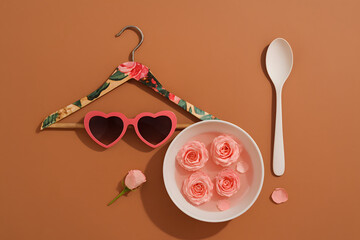 Delicate rose petals floating in a bowl with a spoon on a pink surface