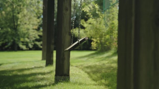 Cinematic moving shot of an empty wooden swing gently swaying in a green park, peaceful childhood playground atmosphere with soft sunlight, shallow depth of field, no people