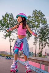 Fototapeta premium A child in a protective sports helmet and knee pads rides in a skate park late at night at sunset