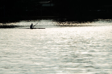 High contrast silhouette of a lone kayaker on a calm lake cove at sunrise representing peace and mindfulness.