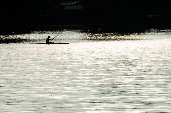 High contrast silhouette of a lone kayaker on a calm lake cove at sunrise representing peace and mindfulness. - Powered by Adobe