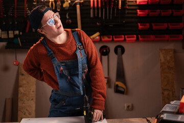 Health Problem Concept. Woman joiner wears workwear in workshop scene with tools hanging on wall...