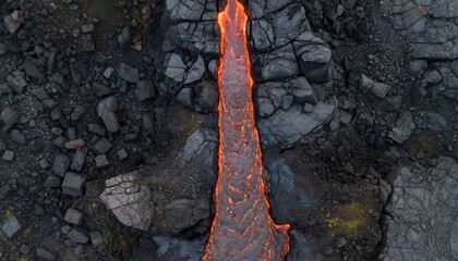 Aerial view of flowing lava stream through dark volcanic rocks and rugged terrain