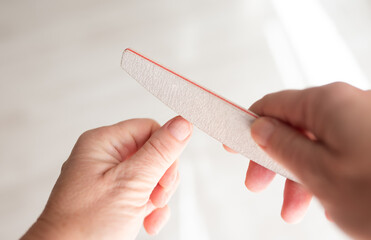 Woman filing fingernails with emery board, bright morning light, beauty salon service, hygiene product brands