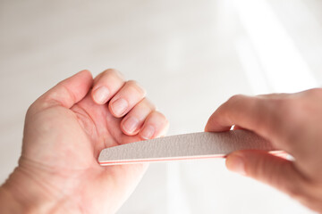 Woman hands filing nails with emery board, bright light and copyspace, beauty salon service,
