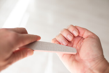Person filing fingernails with professional emery board, soft natural light, beauty studio, skincare clinic