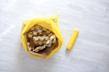 Yellow garbage bag with cardboard waste on light floor, domestic recycling process, eco friendly business