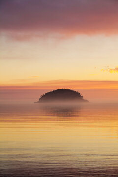 Deception Island, offshore on the coastline of Deception Pass State Park, a silhouette of the island, and mist and layers of colour at sunset.
