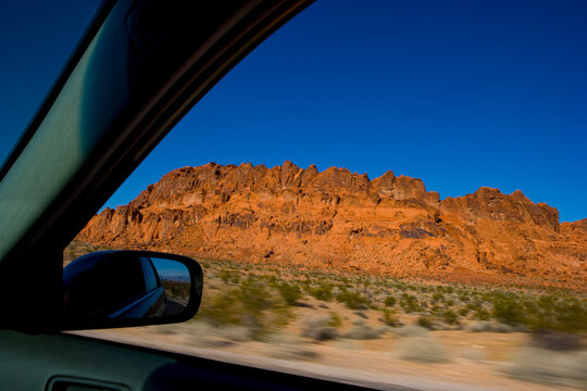 The driver's view of a side mirror, and the open window, a road trip through Red Rock Canyon.
