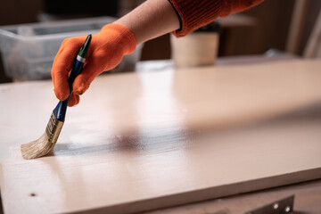 Woman carpenter using brush applying white paint on wooden surface, closeup