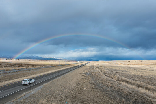 A rainbow in the sky above the highway I-90, a flat landscape and highway through farmland.