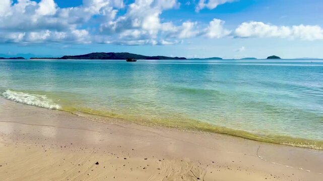 Quiet scene of Hong Van beach with long sandy shore and crystal clear blue sea water. The video is shot from a perspective on the sand, looking out towards small islands and a sky full of white clouds