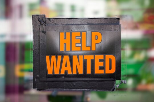 Bright orange "Help Wanted" sign taped to a window, symbolizing job opportunities, hiring, and employment recruitment.