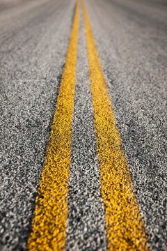 Detailed close-up of yellow double lines painted on an asphalt road, symbolizing travel, direction, and transportation concepts.
