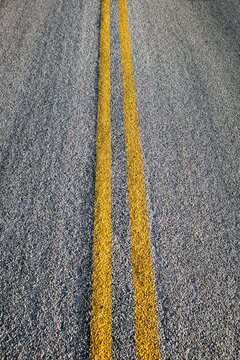 Double yellow lines painted on an asphalt road, symbolizing travel, direction, and transportation concepts.