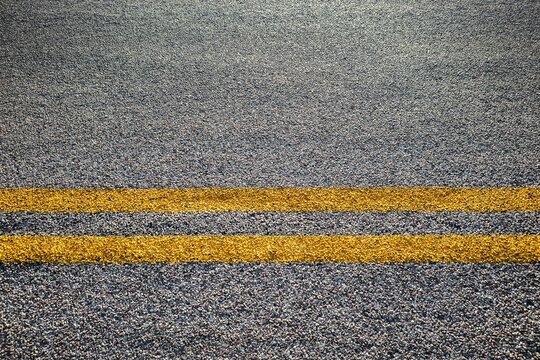 Close-up of double yellow lines painted on an asphalt road, symbolizing rules, safety, and direction.
