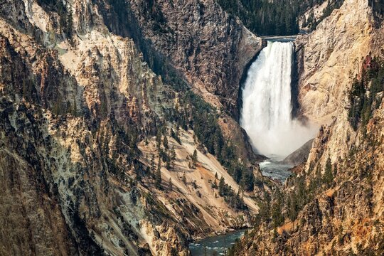 Dramatic view of Lower Falls in Yellowstone National Park, Wyoming, with rugged canyon cliffs and rushing river below.