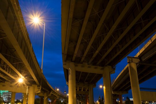 View from below of I-5 freeway overpass at night in Portland, Oregon. Streetlights glow against the deep blue evening sky.