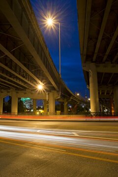 Night view of Interstate 5 freeway overpass in Portland, Oregon with glowing streetlights and vehicle light trails creating motion against a deep blue sky.