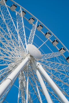 View from below of a Ferris wheel in Seattle, Washington, with white steel beams and gondolas set against a clear blue sky.