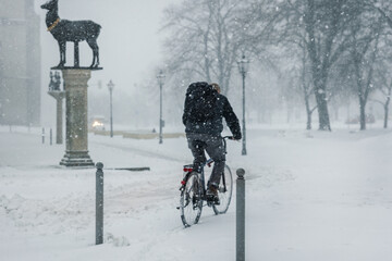 Cyclist rides heavy snowfall winter city altmarkt rathaus under low visibility conditions. Snow covered path cold weather urban solitude highlight daily commute, resilience and sustainable mobility