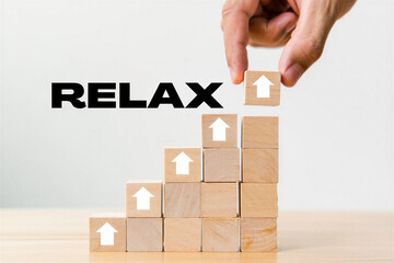 Hand placing wooden block with white arrow on top of stack of blocks with RELAX text on white background for relaxation and calmness concept