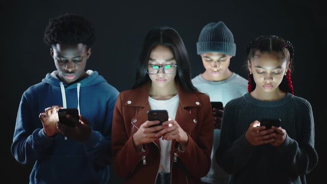 Group of multiethnic teenagers using smartphones in dark studio. Gen Z digital addiction and social media engagement. Lockdown medium shot.