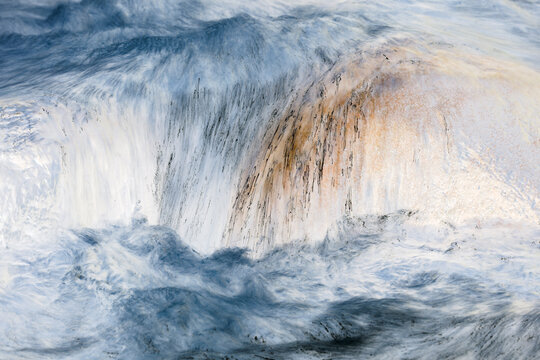 Long exposure of river water flowing over boulders and rocks, impressionist style, brown white and grey colours.