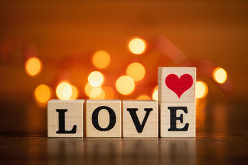 Wooden blocks spelling love with heart on top and bokeh lights in background for valentines day or romantic gesture