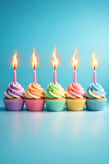 Colorful birthday cupcakes with pastel frosting and lit candles arranged in a row on blue background