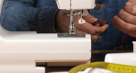 Adult hands threading a sewing machine needle for dressmaking