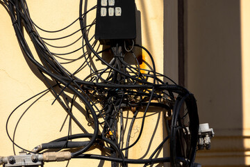 Chaotic bundle of exposed electrical and communication cables mounted on building facade in...