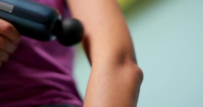 Woman massaging arm muscle with percussion gun