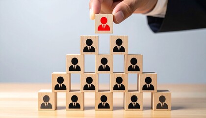 Hand placing a red leader icon at the top of a wooden block pyramid symbolizing corporate hierarchy and leadership