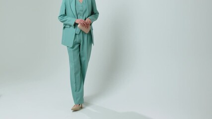 Elegant model posing in mint green three piece tailored suit featuring oversized blazer vest wide leg trousers. Minimalist fashion styling with beige heels clutch bag studio background