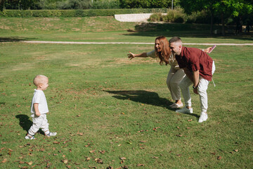 Parents cheering toddler taking first steps on grass