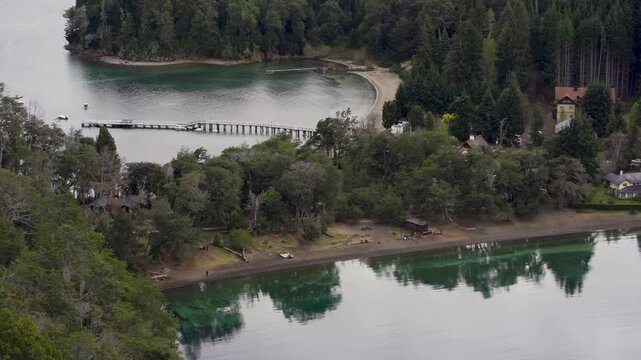 High-angle view of the pristine beaches and turquoise waters of Bah&iacute;a Mansa with a long wooden pier and waterfront villas in Villa La Angostura, Patagonia