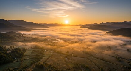 Golden sunlight illuminates dense fog covering a vast valley nestled between rolling mountains at dawn