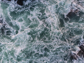 Fototapeta premium Aerial view of turquoise ocean waves crashing against rocks in Mirissa, Sri Lanka