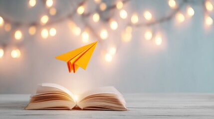 An open book with an illuminated center, featuring a paper airplane flying above, surrounded by soft glowing lights in the background.