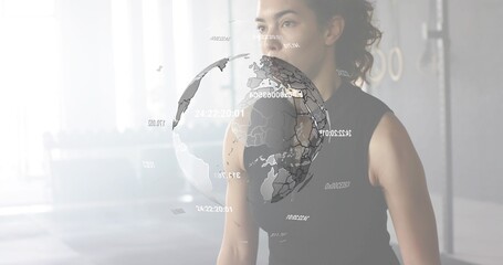 Standing woman wearing dark tank top focusing on digital globe in gym, copy space