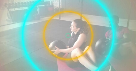 Twisting woman wearing sleeveless black top and shorts on pink mat holding medicine ball at gym