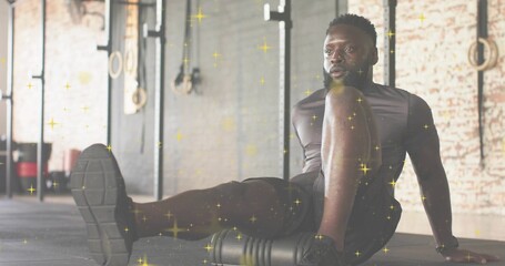 Rolling athlete using foam roller on rubber floor in warehouse gym, in shorts, rig or rings, sparkle